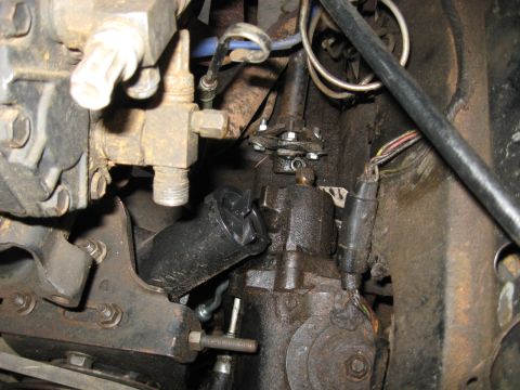 1978 Ford Bronco - Tight engine-bay shot of a grimy power steering gearbox mounted to a rusty frame rail, with the steering shaft rag joint and pinch bolt vis…
