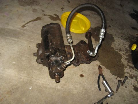 1978 Ford Bronco - A used steering gear box with attached hydraulic lines rests on a stained concrete surface next to tools.