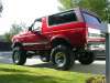 1996 Ford Bronco - A red full-size Ford Bronco with a white removable hardtop parked on a paved driveway, shot from the three-quarter rear. The truck sits on…