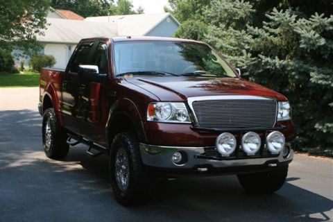 2006 Ford F-150 - A maroon Ford F-150 pickup truck is parked in front of a house and trees.