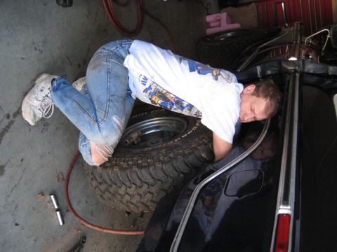 1978 Ford Bronco - A man is seen working on the tire of a black vehicle inside a garage.