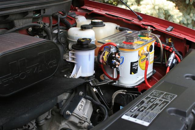 Engine bay with a large aftermarket battery, air intake, and various fluid reservoirs