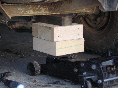 1978 Ford Bronco - A vehicle's frame is elevated by bricks stacked on a jack, with a tire in the background.
