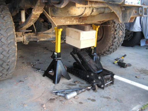 1978 Ford Bronco - The underside of a vehicle is supported by jack stands and a floor jack, with tools nearby.