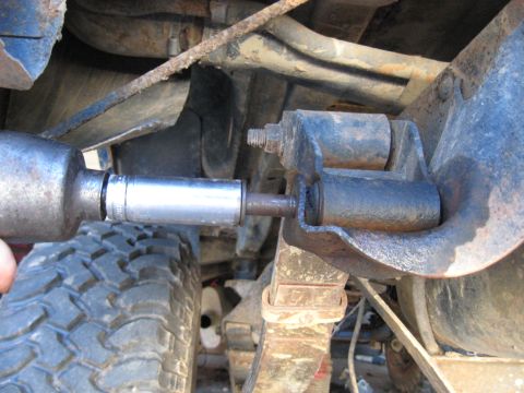 1978 Ford Bronco - A socket wrench is used to adjust a bolt on the suspension system of a vehicle, with a tire in view.