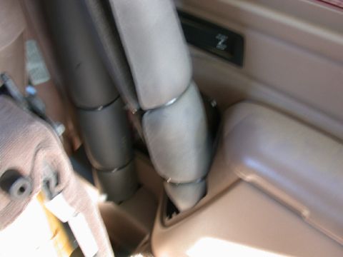 1996 Ford Bronco - Blurry interior close-up of a tan-trimmed cab showing padded roll-bar tubing wrapped in gray covers running down beside a tan rear wheel-we…