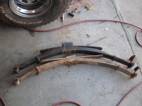 1978 Ford Bronco - Leaf springs and a tire are laid out on a concrete floor with tools nearby.