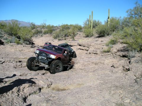 1986 Toyota Hilux - A modified 1996 Toyota Tacoma navigates a challenging rocky trail with other vehicles in the background.