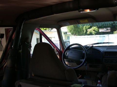 1996 Ford Bronco - Interior of a 1990s Ford truck/SUV shot from the rear over the cloth front bucket seats, showing the padded roll bar, gray dash, four-spoke…