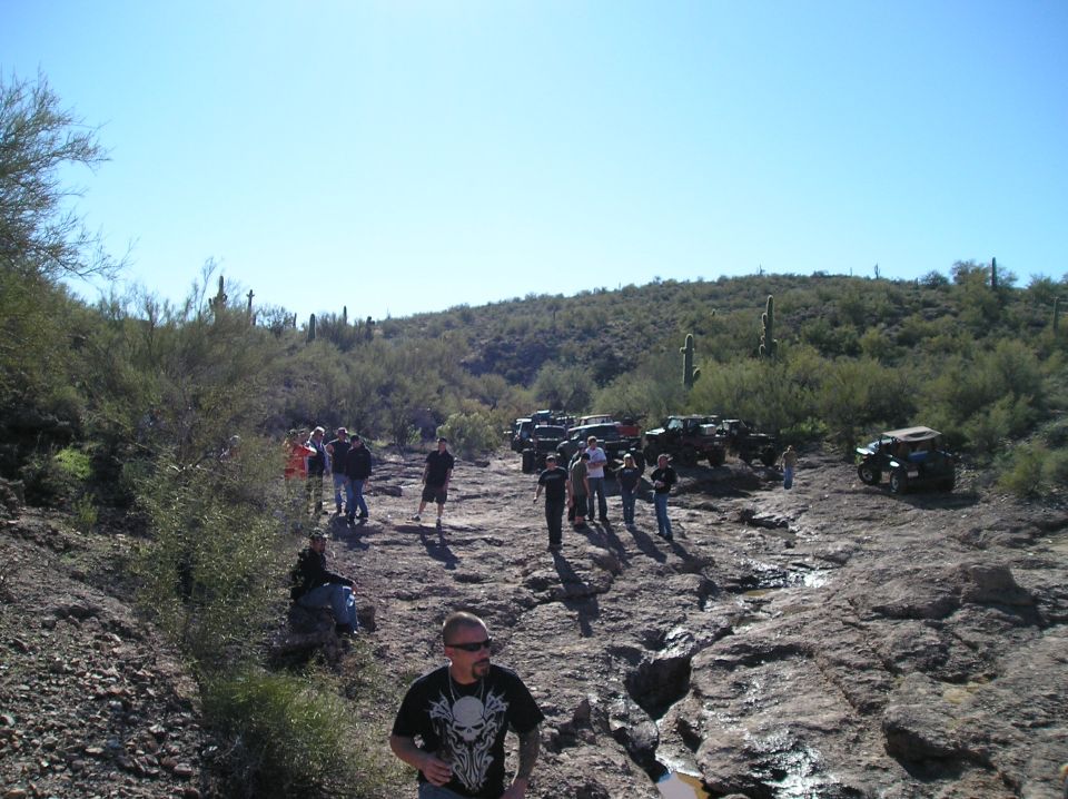 Group of people gathered around several off-road vehicles on a rocky desert trail
