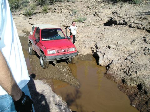 1986 Toyota Hilux - A red SUV navigates a muddy obstacle on an off-road trail.