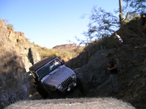 1986 Toyota Hilux - A silver Jeep Wrangler tackles a challenging off-road course on a sunny day.