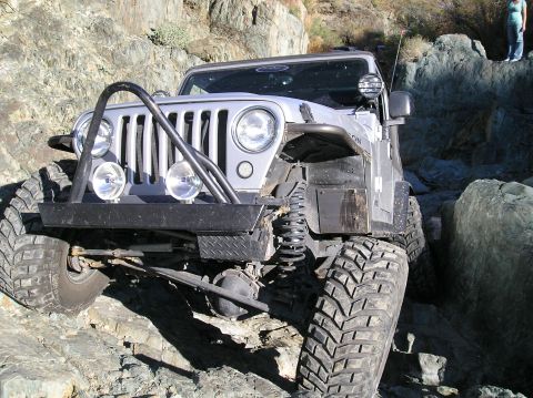 1986 Toyota Hilux - A silver Jeep Wrangler is shown off-roading over large rocks.