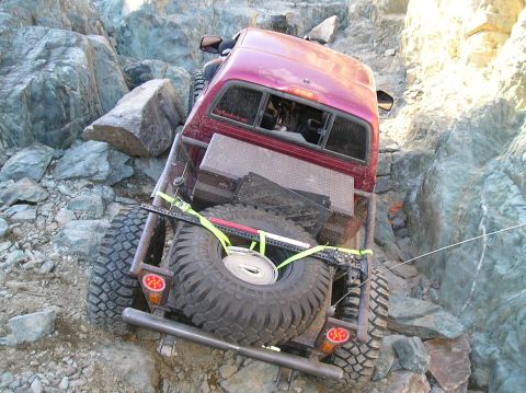 1986 Toyota Hilux - Pickup truck navigating a difficult rocky trail, showing its rear end and spare tire.