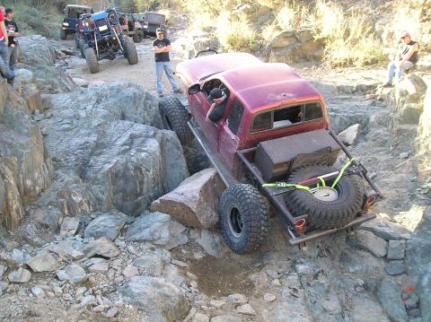 1986 Toyota Hilux - Several off-road vehicles navigate a rocky trail, with one truck carefully maneuvering over large boulders.