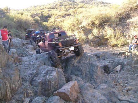 1986 Toyota Hilux - Multiple off-road vehicles traverse a challenging rocky terrain on a sunny day.