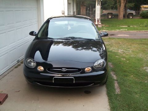 1999 Ford Taurus - The front view of a black sedan parked on a concrete driveway next to a garage.