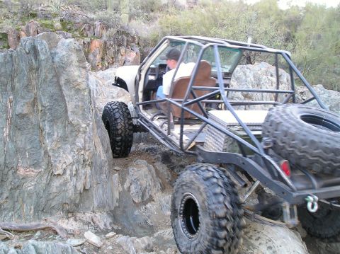 1986 Toyota Hilux - Custom buggy with roll cage climbs over large rocks in a desert landscape.