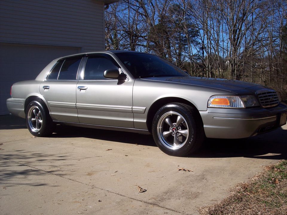 Silver sedan parked in a driveway. It has aftermarket wheels and appears to be a 2000 Ford Crown Victoria