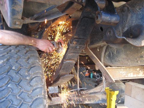 1978 Ford Bronco - A person modifies a vehicle's suspension system by cutting a leaf spring with an angle grinder.