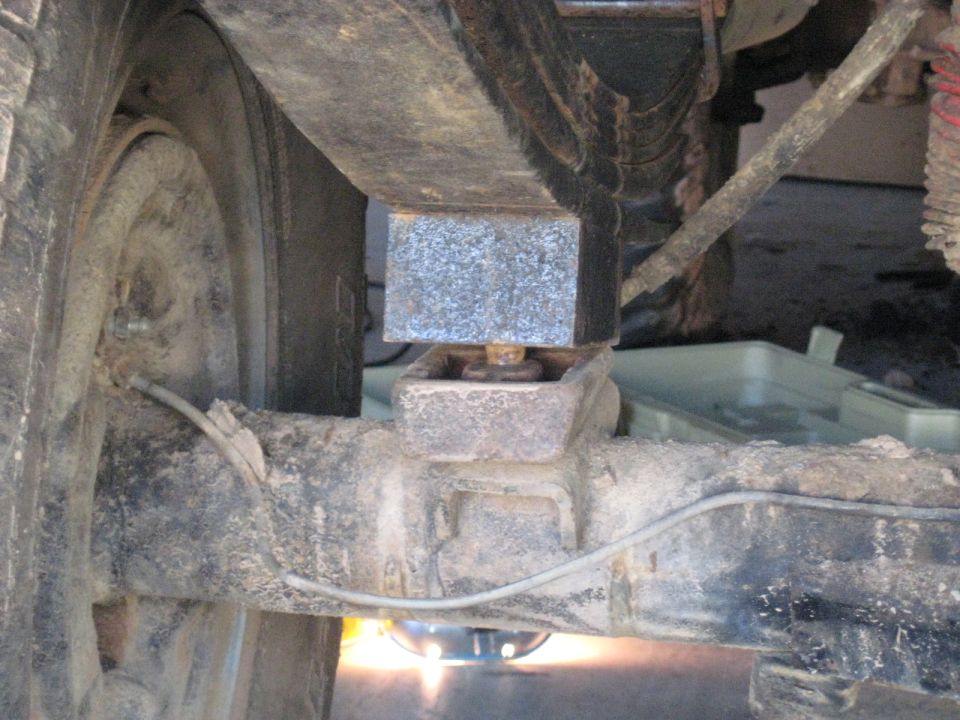 Close-up of a metal block inserted between a leaf spring and the axle of a vehicle