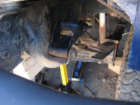 1978 Ford Bronco - Vehicle's rear suspension leaf spring and shackle assembly, with a jack providing support.
