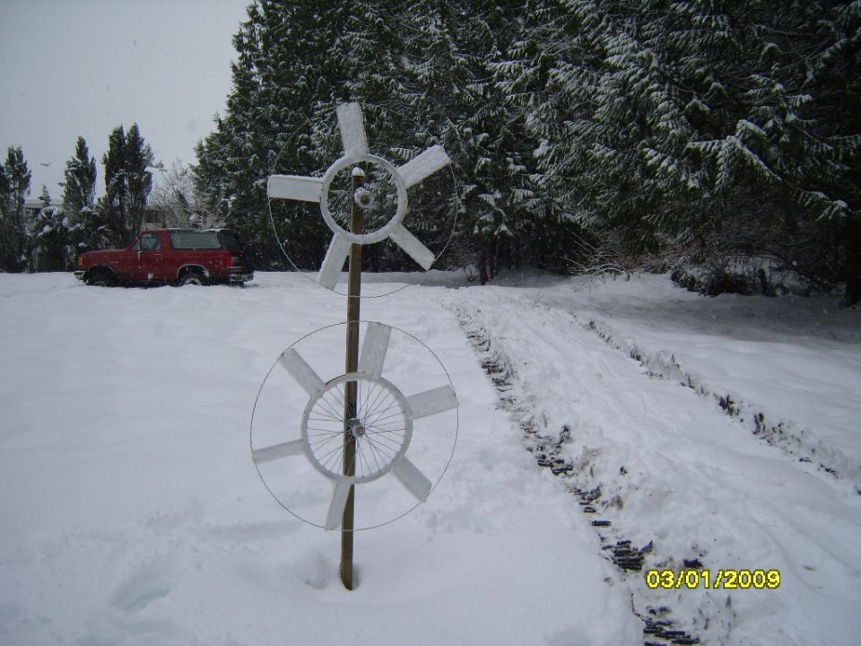 Red SUV parked in a snowy yard with a homemade wind turbine in the foreground