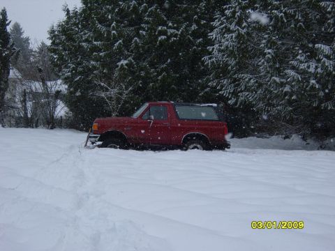 1989 Ford Bronco - A red SUV is stuck in deep snow with snow falling around it.