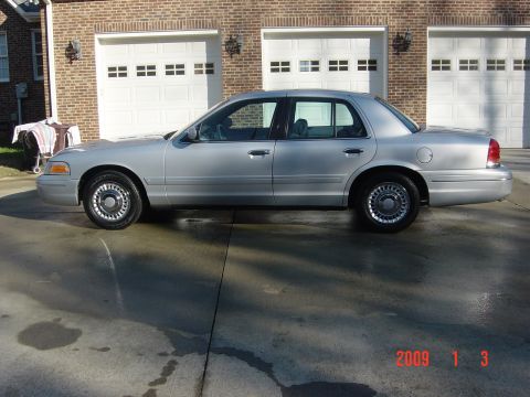 2000 Ford Crown Victoria - A silver sedan is parked in front of a brick house with a three-car garage. The date 2009 is visible in the lower right corner.