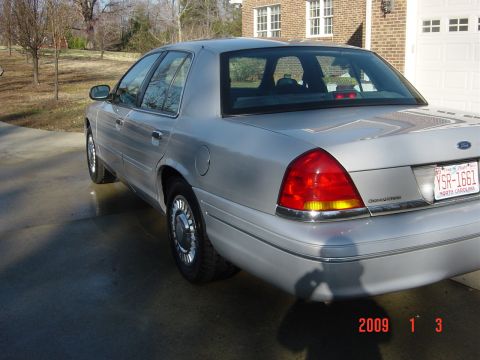 2000 Ford Crown Victoria - A silver 2000 Ford Crown Victoria is parked on a driveway next to a brick house.