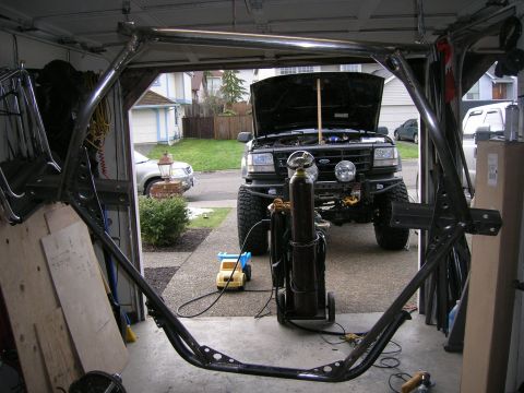 1996 Ford Bronco - Custom roll cage frame being fabricated in a garage, with a Ford Bronco visible outside.