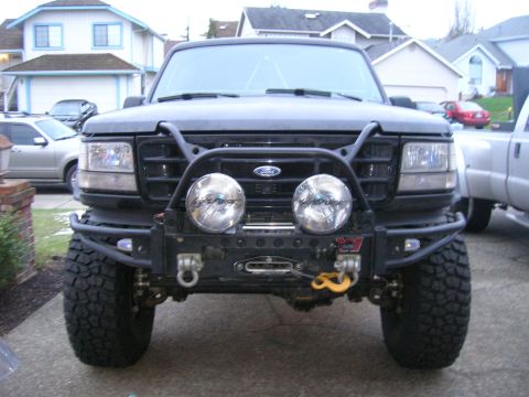 1996 Ford Bronco - Frontal view of a black Ford truck a heavy-duty aftermarket bumper with a winch and two large auxiliary lights.