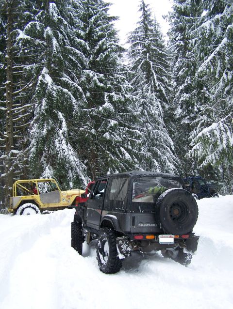 1988 Suzuki Samurai - A black 1988 Suzuki Samurai navigates a snowy forest road, with another off-road vehicle visible in the background.