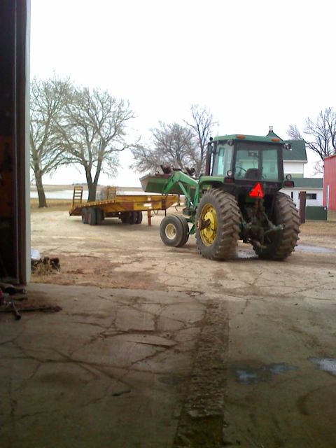 1992 Ford Bronco - A green tractor with a front loader is hitched to a trailer, parked outside a barn on a cloudy day.