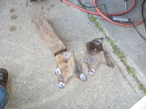 1978 Ford Bronco - Two old, rusty metal brackets and a piece of wood lie on a concrete surface next to an air hose.