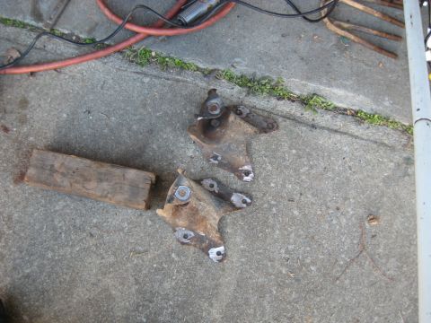 1978 Ford Bronco - Two rusty metal vehicle suspension parts lie on a concrete surface next to a wooden block.