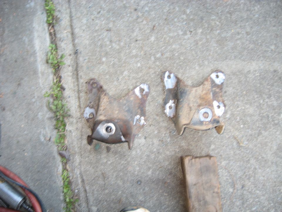 two rusty metal brackets with holes, one has weld marks