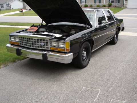 1987 Ford Crown Victoria LTD - A black sedan with its hood open, parked on an asphalt driveway.