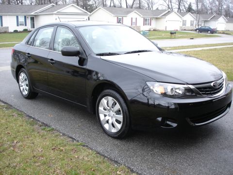 2008 Subaru Impreza - A black sedan is parked on a wet driveway in front of a row of houses.