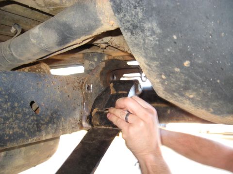 1978 Ford Bronco - Hands work on the suspension of a vehicle, focusing on the leaf spring and frame area.