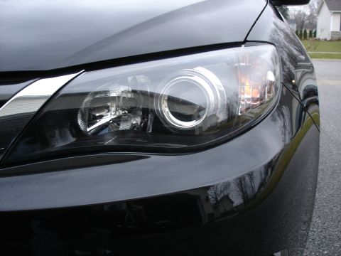 2008 Subaru Impreza - The front passenger side headlight of a black Subaru is shown, with a reflection of a house in the background. The page claims it's a 2008…