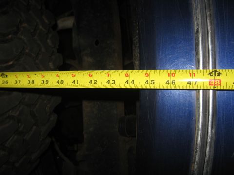 1978 Ford Bronco - A measuring tape is used to assess the clearance of a large tire against a blue vehicle body panel.
