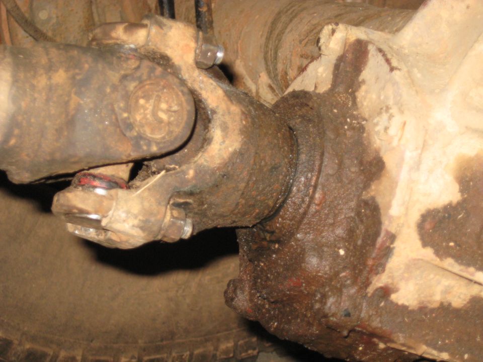 Close-up of a rusty driveshaft U-joint and differential under a vehicle