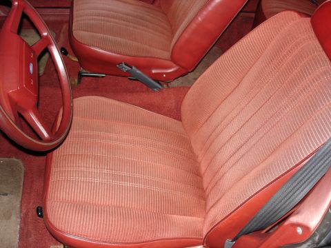 1987 Ford LTD Crown Victoria - Interior view of a red cloth-and-vinyl split bench front seat shot from the passenger door, with matching red carpet and a red four-spoke F…