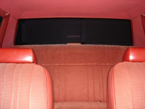 1987 Ford LTD Crown Victoria - View from the front seats toward the red ribbed-velour rear bench of a sedan, showing matching red headliner, rear package shelf and the de…