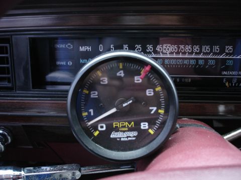 1987 Ford LTD Crown Victoria - Tight interior shot of an Auto Meter Autogage 0-8000 RPM tachometer with a red shift-light indicator set near 5,000, mounted on top of the…