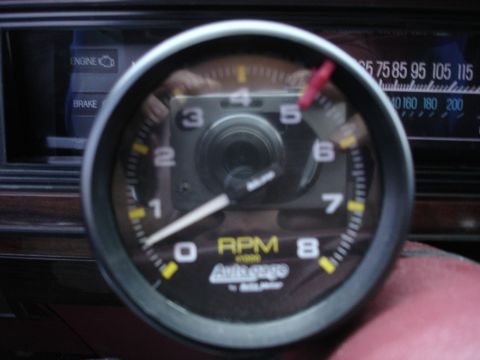 1987 Ford LTD Crown Victoria - Extreme close-up of a dash-mounted Auto Meter Autogage 0-8000 RPM tachometer with a red shift-light pointer, the photographer's compact cam…