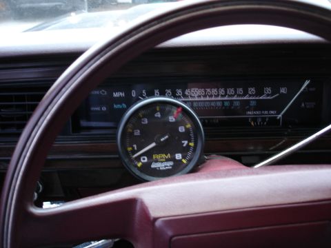 1987 Ford LTD Crown Victoria - Interior dash view through a burgundy steering wheel showing an aftermarket Auto Meter Autogage 0-8000 RPM tachometer with a red shift-ligh…