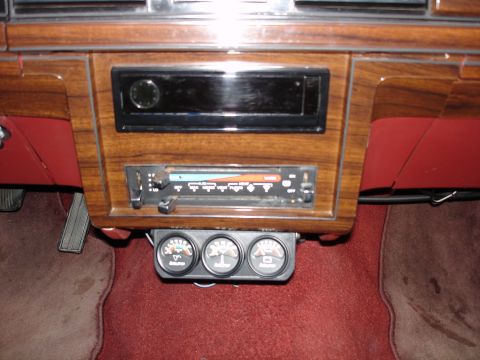 1987 Ford LTD Crown Victoria - The interior of a classic car shows a wooden dashboard with a car stereo and three gauges mounted below it. The car has red interior accent…