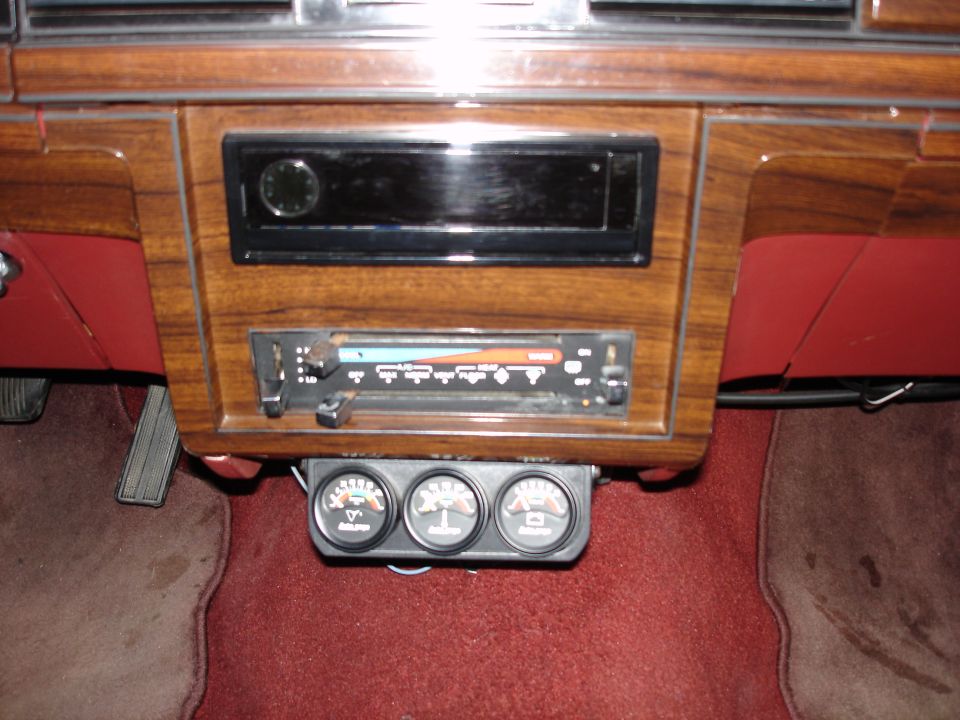 Interior of a classic car with wood grain dashboard, stereo, and three gauges.